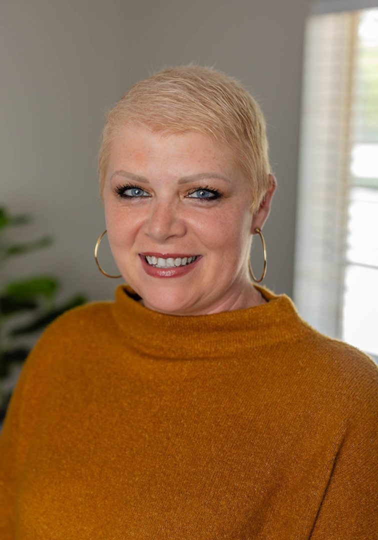 Smiling woman in orange sweater, hoop earrings.